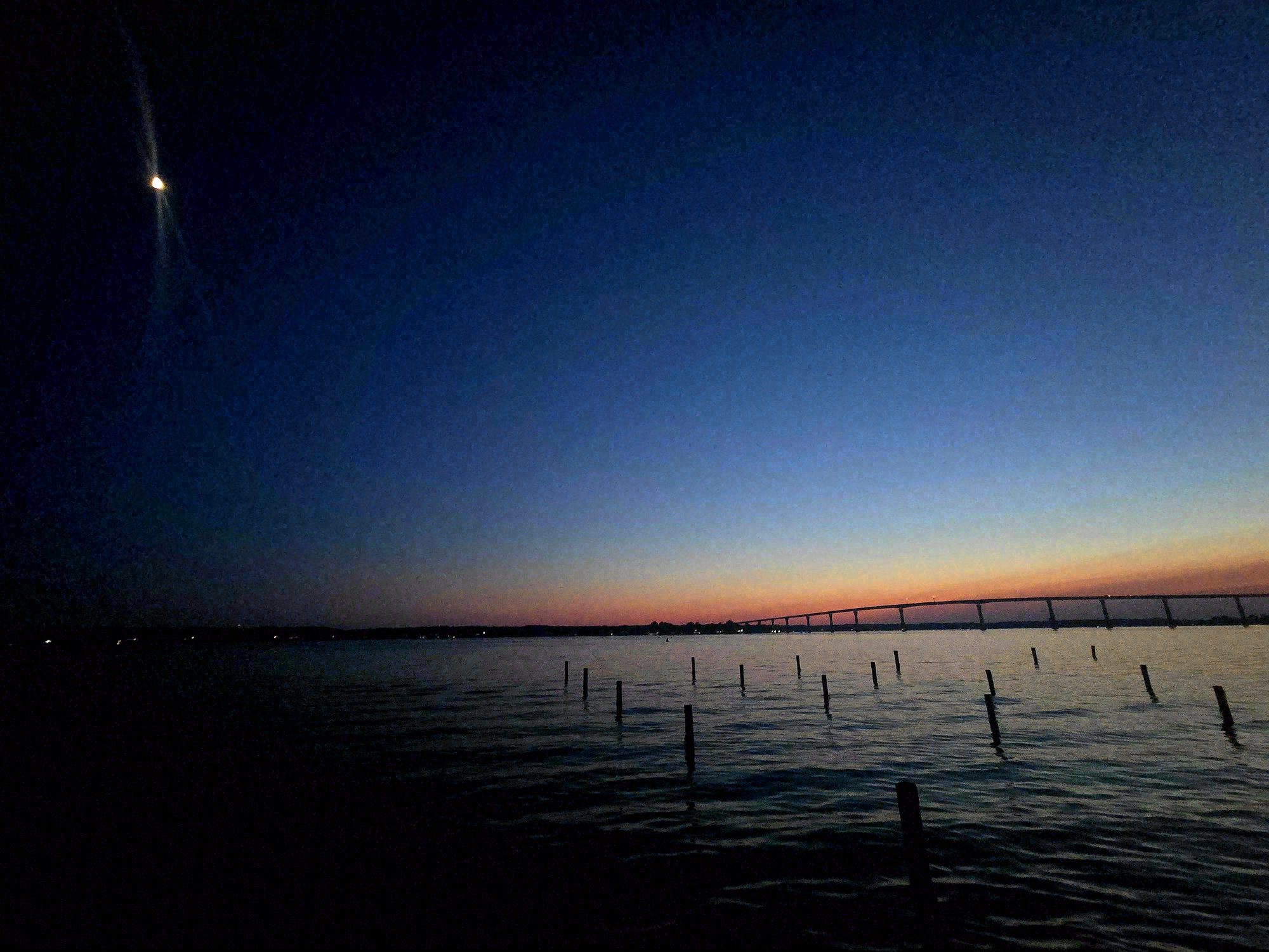 The same bridge ten seconds later. The peach has cooled and the moon hangs low above the bridge. The horizontal of the railing remains, the structure of the frame unchanged, the conditions entirely different.
